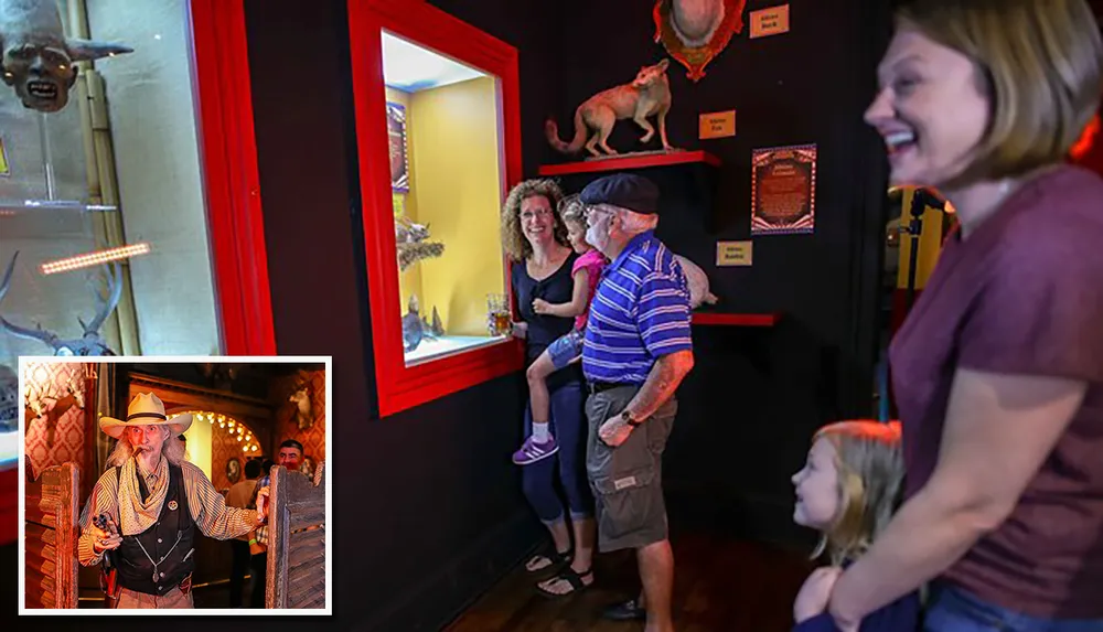 A group of people including children are looking at a display containing a bat-like creature in a brightly lit exhibit with an inset image of a man dressed as a cowboy
