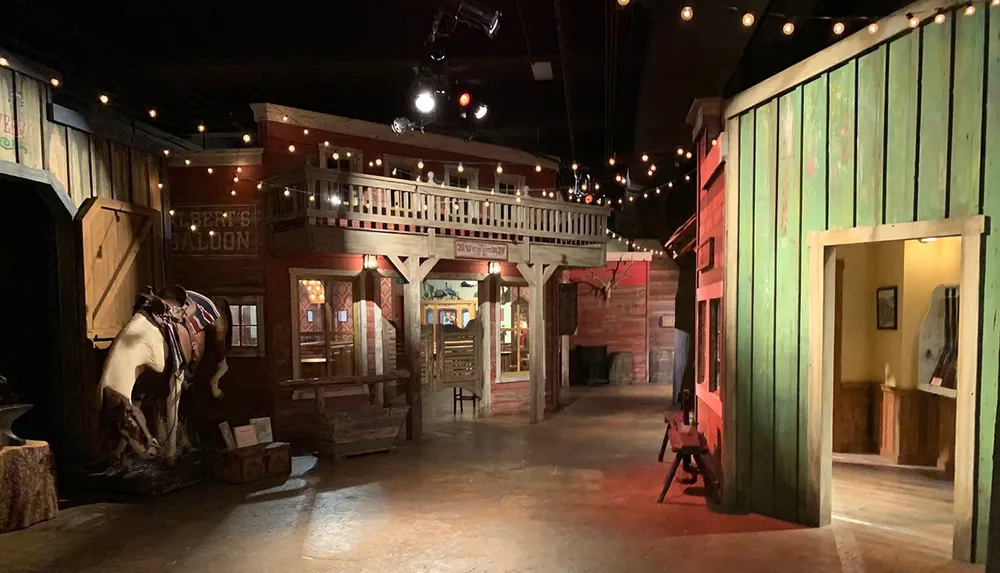 The image depicts a dimly lit Western-themed indoor set with string lights a saloon facade and a horse figure