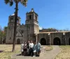 A group of people is posing for a photo in front of an old Spanish colonial church with a clear blue sky above them