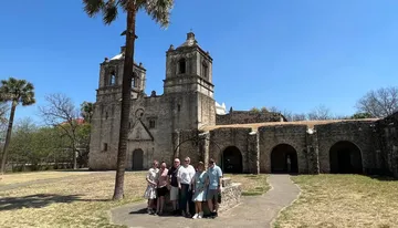 A group of people is posing for a photo in front of an old Spanish colonial church with a clear blue sky above them.