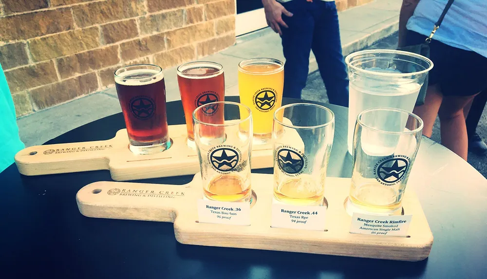 A flight of craft beer samples is presented on a wooden paddle with descriptive labels at a tasting event