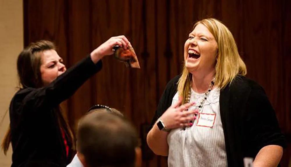 A person is playfully throwing a slice of pizza at a laughing individual during what appears to be a social event