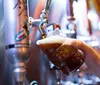 A person is pouring a dark beer from a tap into a branded glass with a foamy head forming on top