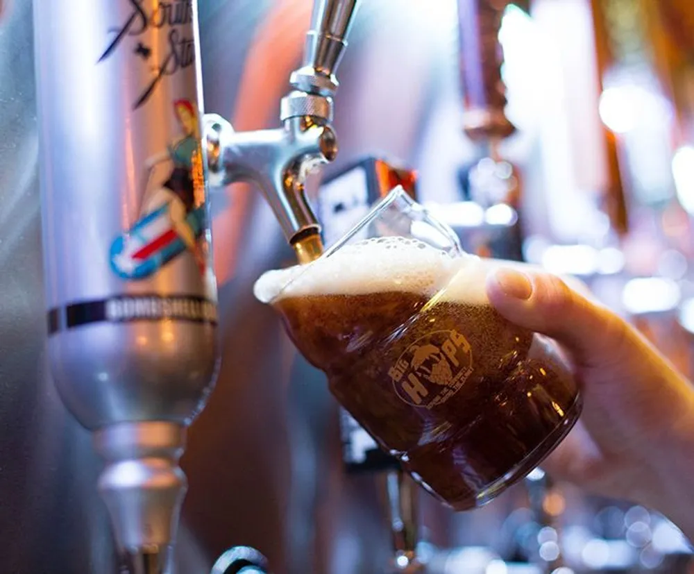 A person is pouring a dark beer from a tap into a branded glass with a foamy head forming on top