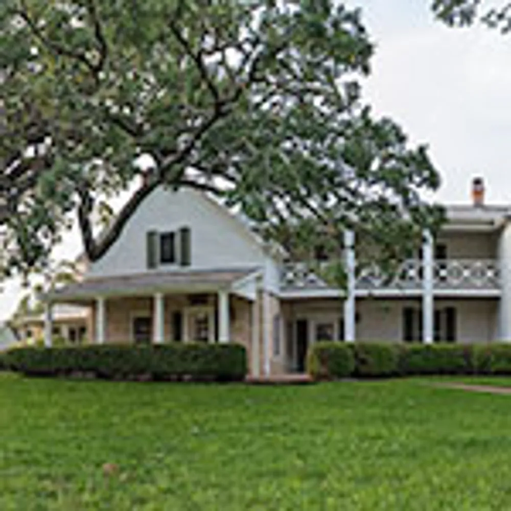 The image features a multi-story house with a unique steeply-pitched roof and several dormer windows against a backdrop of blue sky and clouds