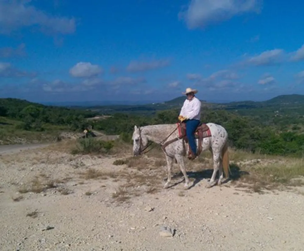 A person in a cowboy hat is riding a horse on a rugged trail with a scenic landscape in the background