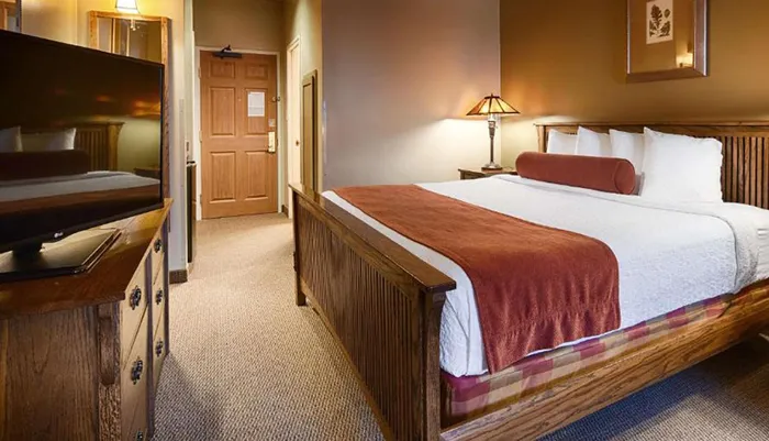 The image shows a neatly arranged hotel room with a large bed a television and warm lighting