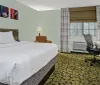 A modern hotel room featuring a neatly made bed colorful artwork on the wall patterned carpet a desk with an office chair and a window air conditioning unit beneath a closed window