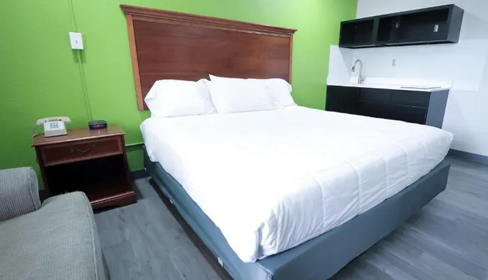 The image shows a neatly made bed in a hotel room with green walls wood and black furnishings and a gray floor