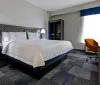The image shows a well-kept hotel room with a large bed contemporary furniture and a brightly lit window