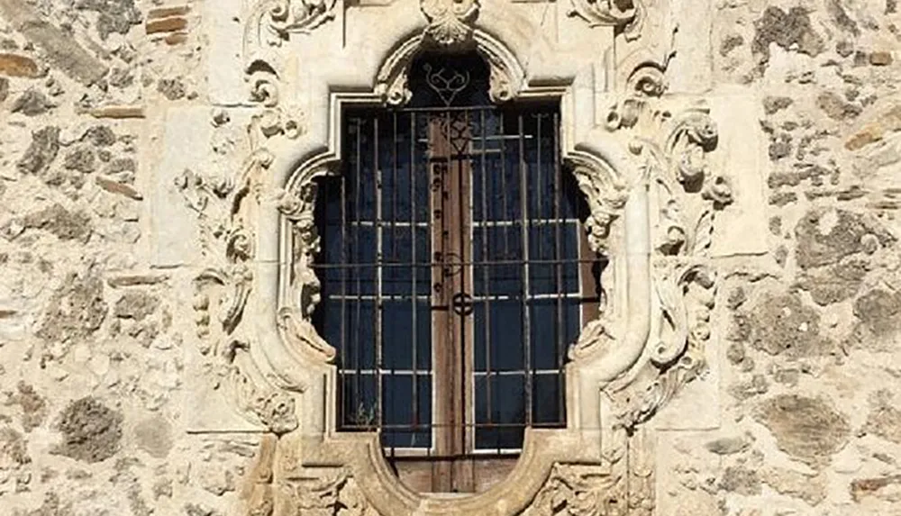 The image showcases a baroque-style ornate window with intricate stone carvings and iron bars set into a textured stone wall