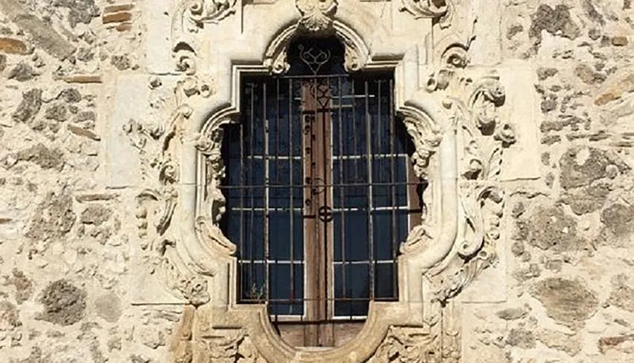 The image showcases a baroque-style ornate window with intricate stone carvings and iron bars set into a textured stone wall.