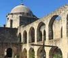 The image shows the historical architecture of an old stone mission with a dome and arches under a clear blue sky