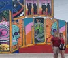 A couple is posing in front of a vibrant and colorful mural with the text Greetings from incorporated into the design