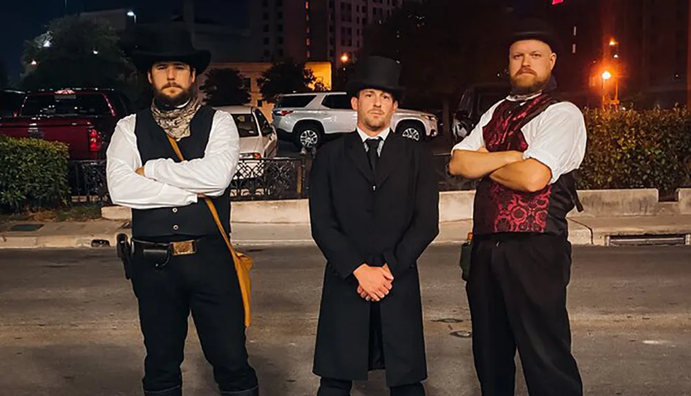 Three men stand confidently in historic or costume attire reminiscent of the Wild West era with the background revealing a modern urban night setting