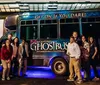 A group of people are posing for a photo in front of a bus that is advertised for a ghost tour in San Antonio