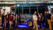 A group of people are posing for a photo in front of a bus that is advertised for a ghost tour in San Antonio.