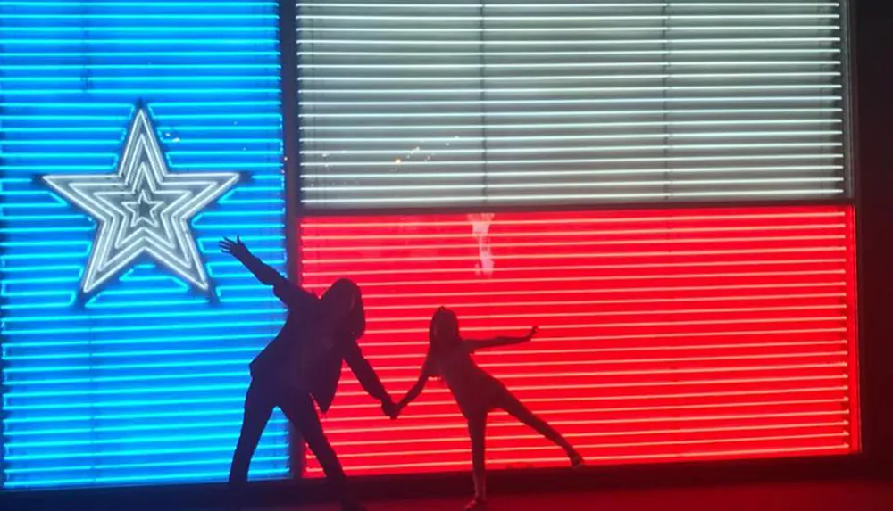 Two silhouetted figures are playfully posing in front of a neon-lit backdrop featuring blue and red vertical stripes and a lit-up star symbol