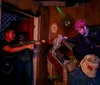 A group of people appear terrified and scream while gathered around a table with a fake gory figure as part of what looks like a haunted house or horror-themed attraction