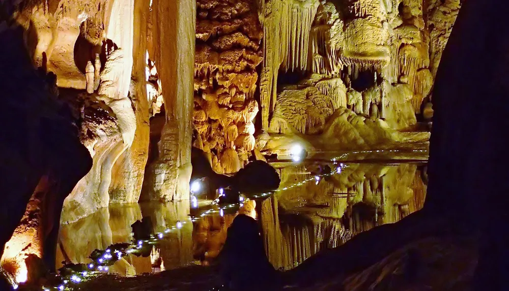 The image shows a luminous underground cave with intricate stalactites and stalagmites reflecting beautifully in a still pool of water