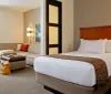 The image shows a neatly organized hotel room with a large bed and a separate sitting area highlighting a comfortable and welcoming arrangement for guests