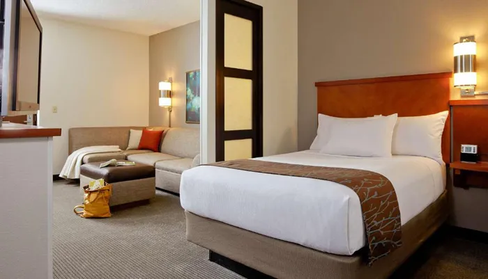 The image shows a neatly organized hotel room with a large bed and a separate sitting area highlighting a comfortable and welcoming arrangement for guests