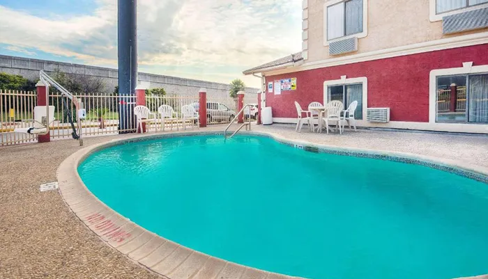 The image shows a small outdoor hotel swimming pool with surrounding chairs and a fenced-off area under a partly cloudy sky