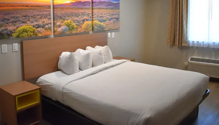 A neatly made bed sits in a hotel room with a large landscape painting above the headboard