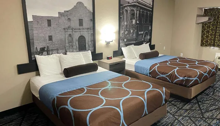 The image shows a hotel room with two beds each adorned with a brown and blue patterned bedspread flanked by large black and white photographs on the wall