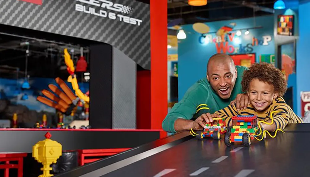A child and an adult are joyfully engaging with a colorful Lego structure at a play area designated for building and testing Lego creations
