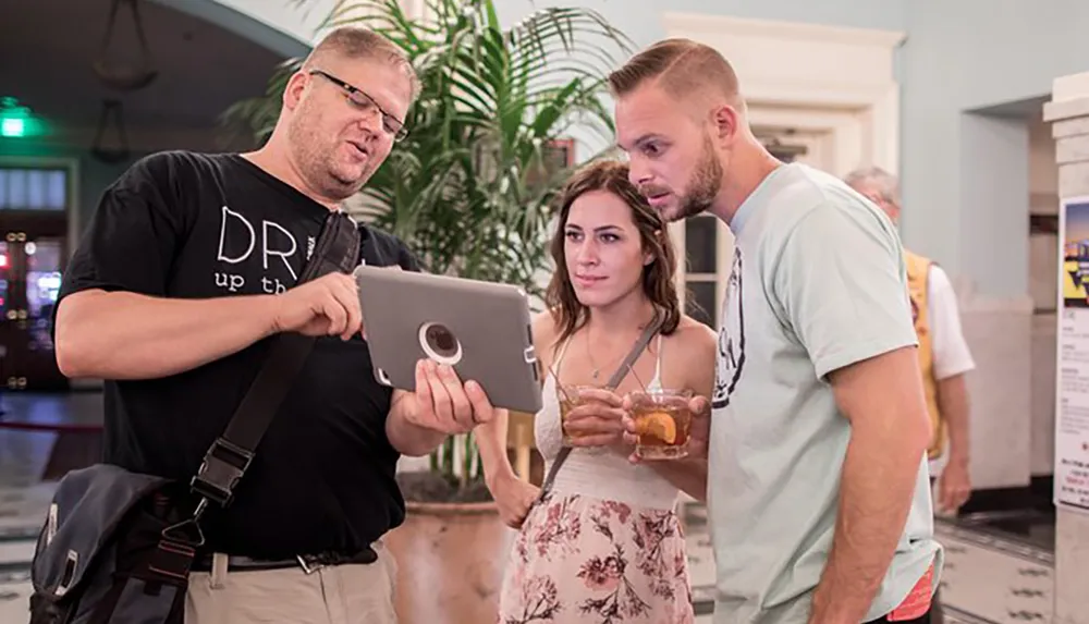 Three people are intently looking at a tablet that one of them is holding
