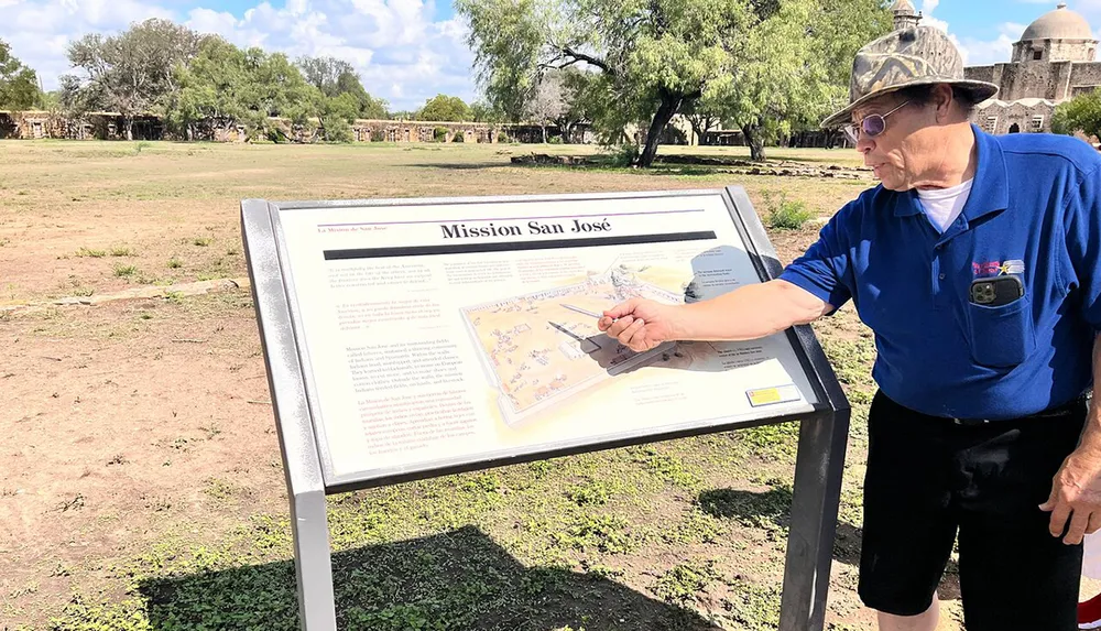 A person is reading and pointing at an informational display about Mission San Jos at a historical site