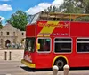 A red double-decker sightseeing tour bus is parked on the street advertising hop-on hop-off services and air conditioning with people seated on the upper open-air level