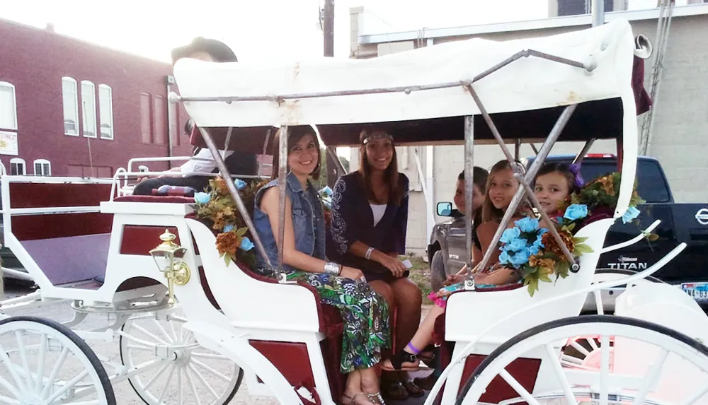 Four passengers are smiling while seated in a decorated horse-drawn carriage on an urban street