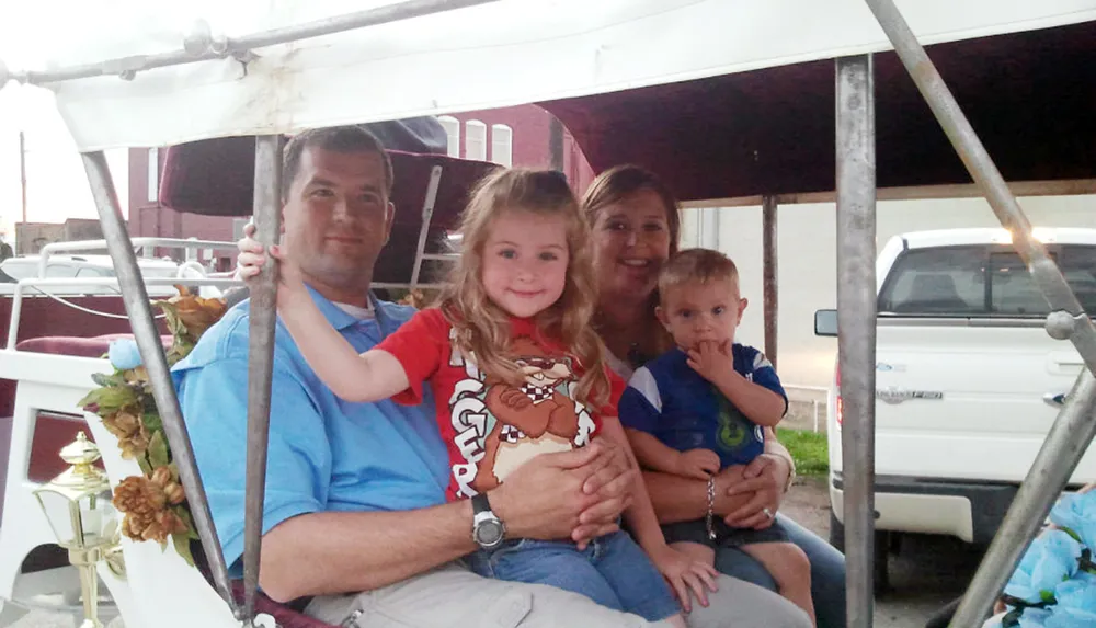 A family of four is smiling for a photo while seated in a white carriage decorated with flowers