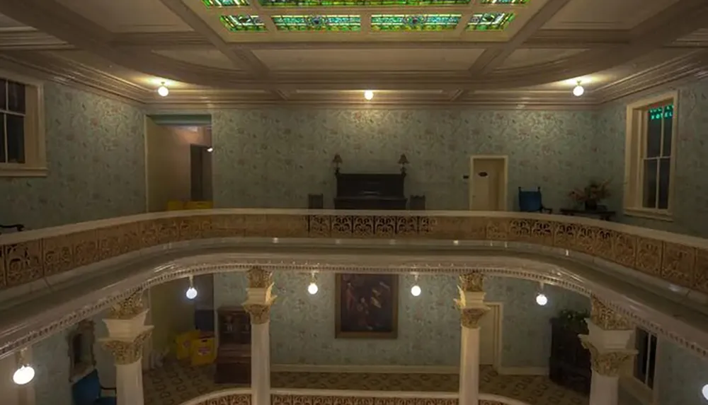 The image shows an elegant interior featuring a balcony with ornate railings classical columns decorative ceiling panels and pendant lighting