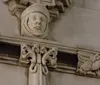 The image shows an architectural detail featuring a carved stone face framed by decorative elements including winged figures on a buildings faade