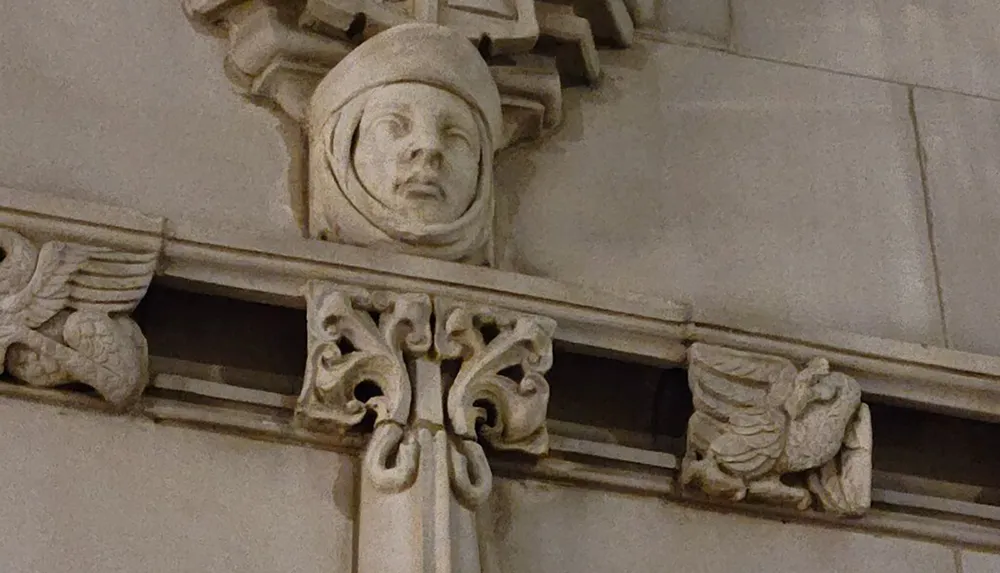 The image shows an architectural detail featuring a carved stone face framed by decorative elements including winged figures on a buildings faade