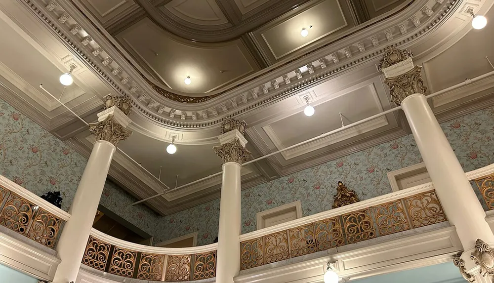The image shows an elegant interior with ornate ceilings decorative columns and a balcony with an intricate railing design