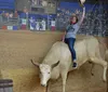 A focused rider in a blue shirt and cowboy hat is galloping on a brown horse in an equestrian arena