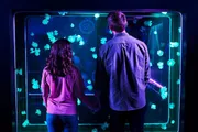 Two people are holding hands while looking at glowing jellyfish in an aquarium.