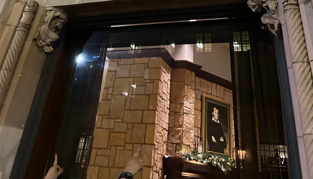 The image shows an interior view of a room with ornate stonework and a portrait hanging on the wall as seen through a window framed by classic architectural elements with a hand pointing towards the bottom left corner