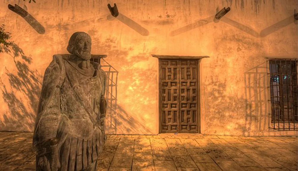 The image depicts a statue of a bearded figure in historical attire standing near an ornate wooden door cast in warm light with shadows of flying doves and tree branches