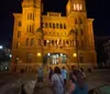 The image shows a group of people walking towards a grand illuminated building at night with a blurred effect suggesting motion or a low-light capture