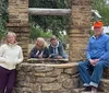 Four people are posing for a photo at an old stone well with three grouped together inside the wells frame and one standing to the side