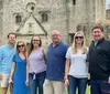 A group of six individuals are posing for a photo in front of an old stone building with historical architecture