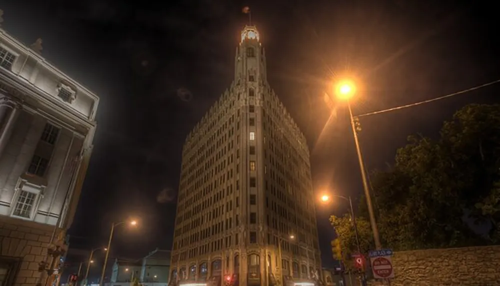 The image depicts a night scene of an illuminated tall historic-looking building with a lighted spire surrounded by streetlights and a dark sky