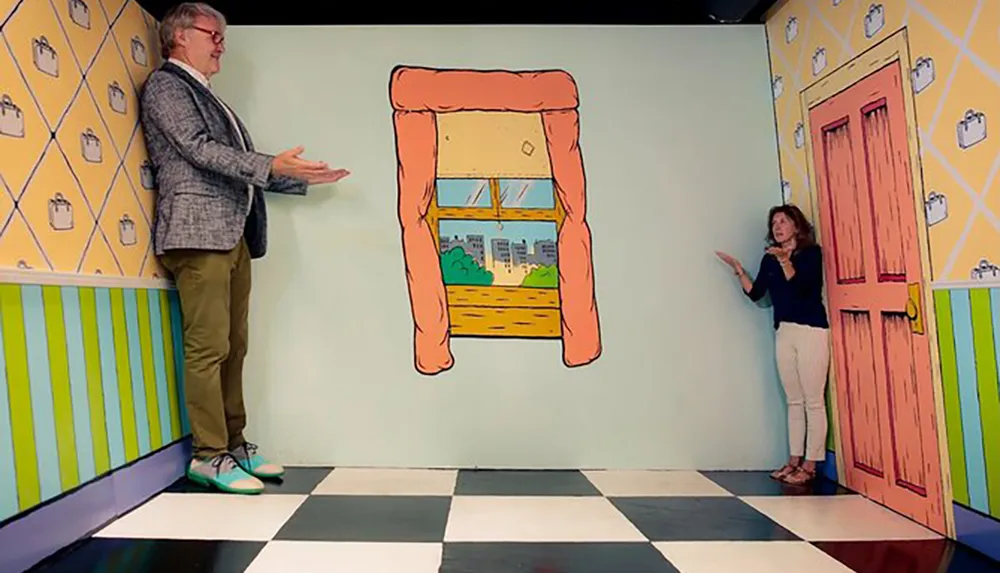 The image shows an optical illusion art installation where a man and a woman appear to be standing in a distorted room that makes the man on the left seem like a giant compared to the diminutive woman on the right