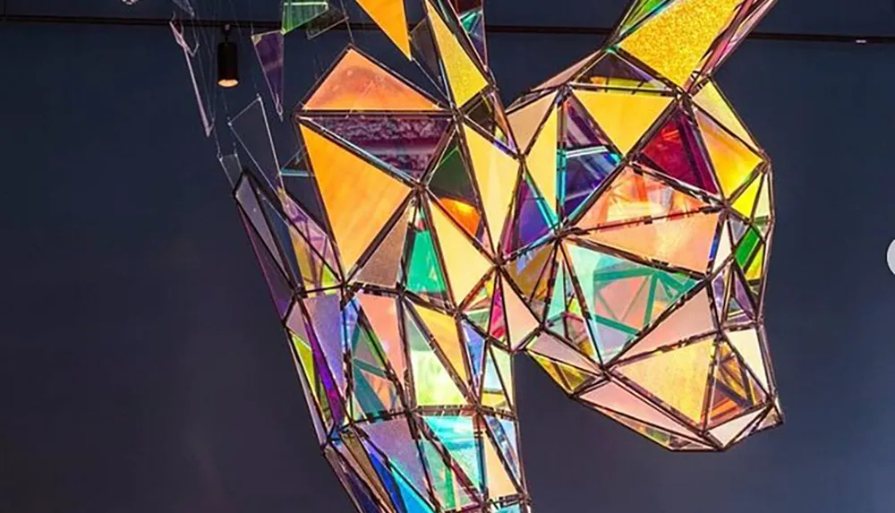 The image features a colorful geometric stained-glass sculpture suspended in mid-air against a dark background