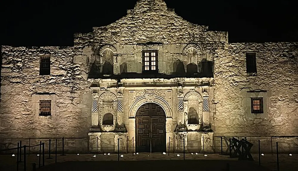 The image shows the illuminated facade of the historic Alamo mission at night